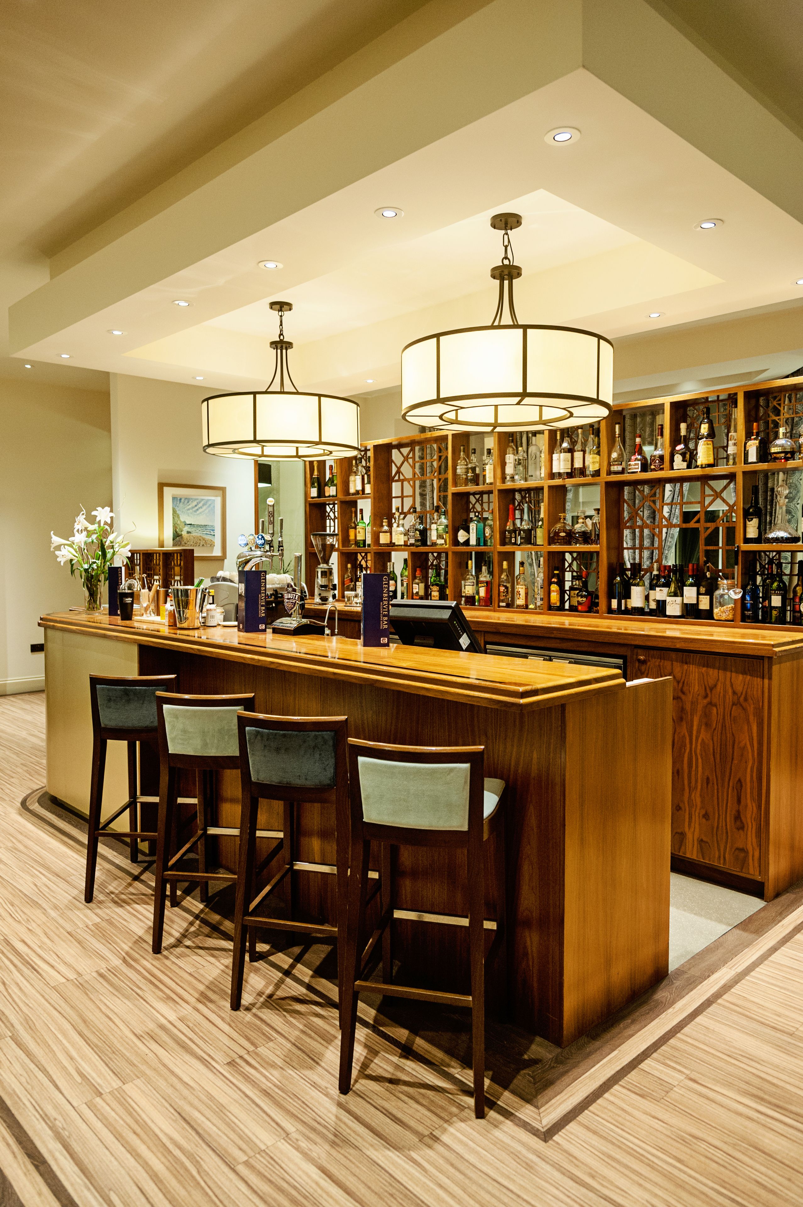 A bar area with wooden bar stools, a counter, and shelves stocked with bottles.