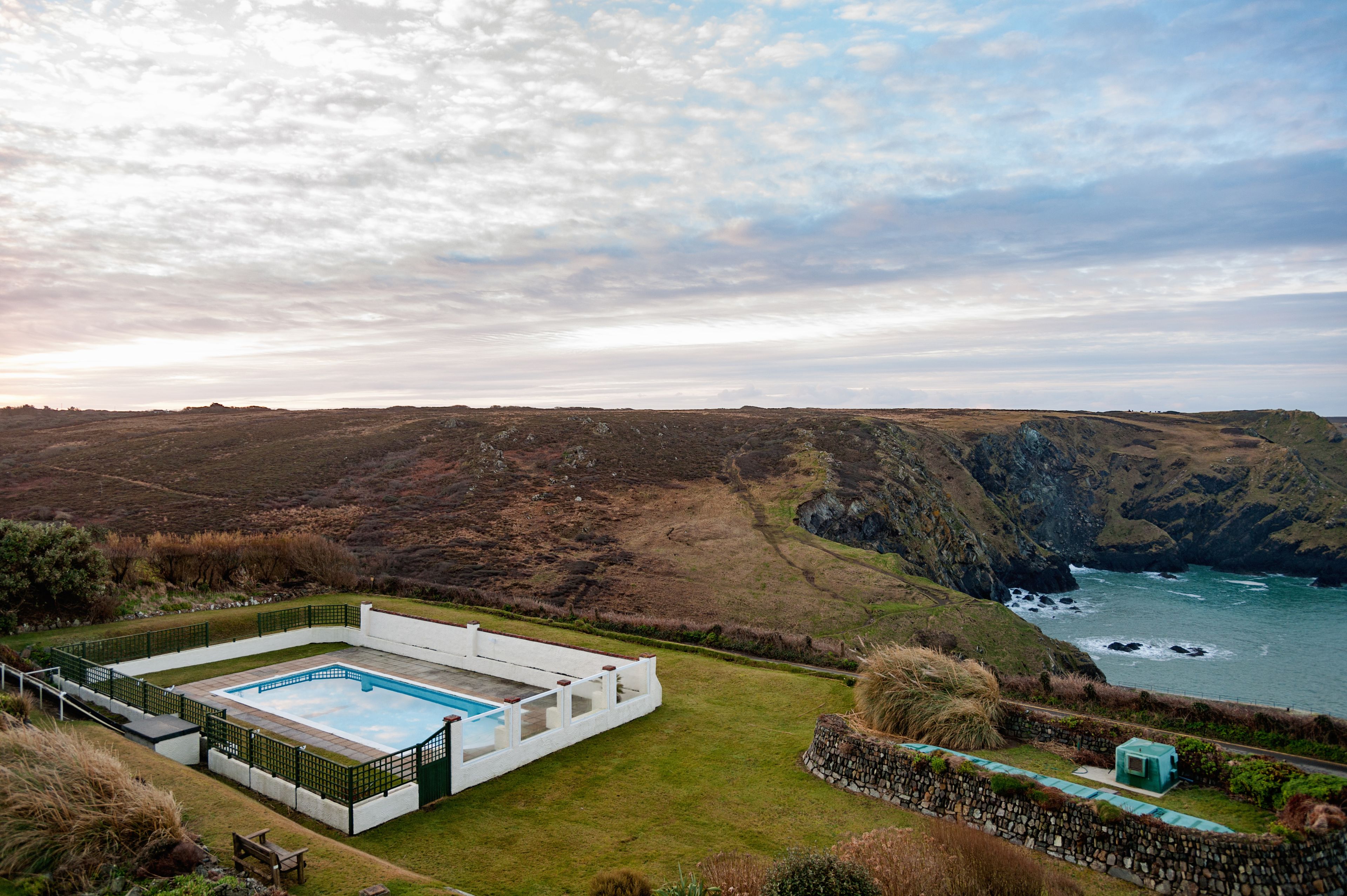 A modern pool house with a rectangular pool, surrounded by a stone wall and a grassy area.