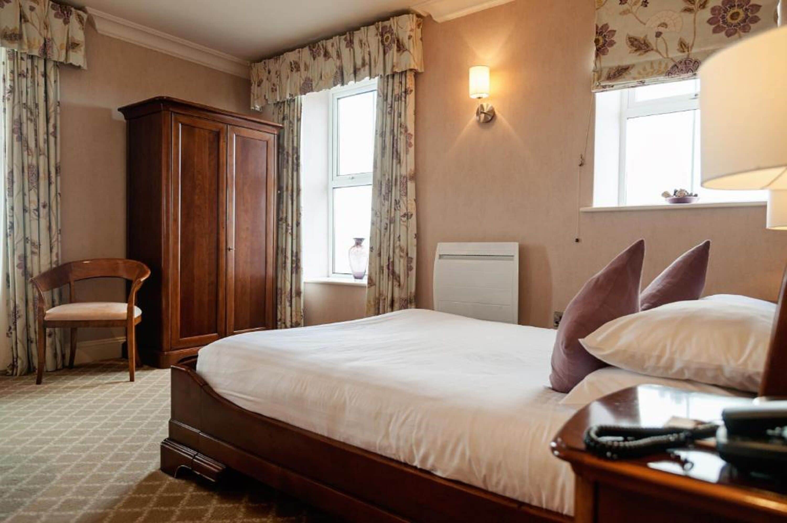 A bedroom with a wooden bed, a nightstand, a chair, a wardrobe, and a window with curtains.