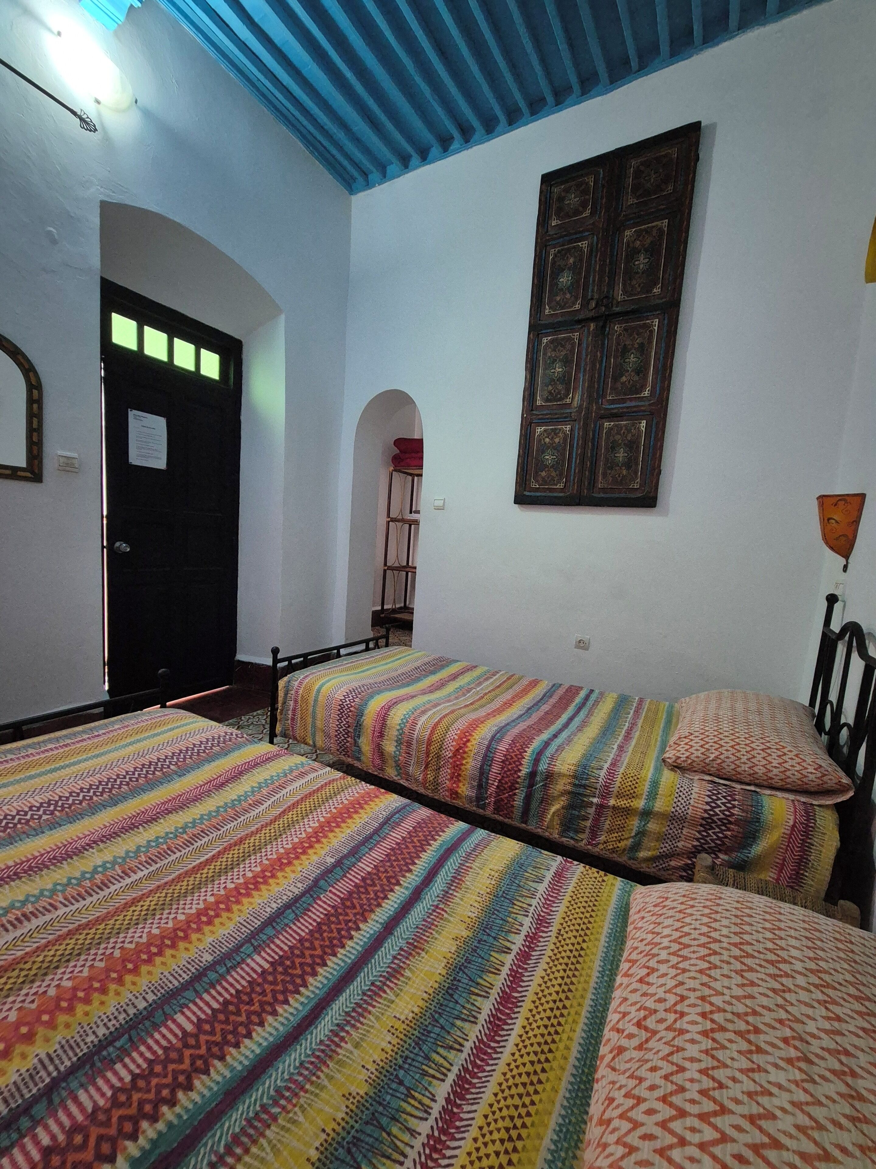A room with two beds, a wooden door, a wall-mounted light fixture, and a decorative panel.