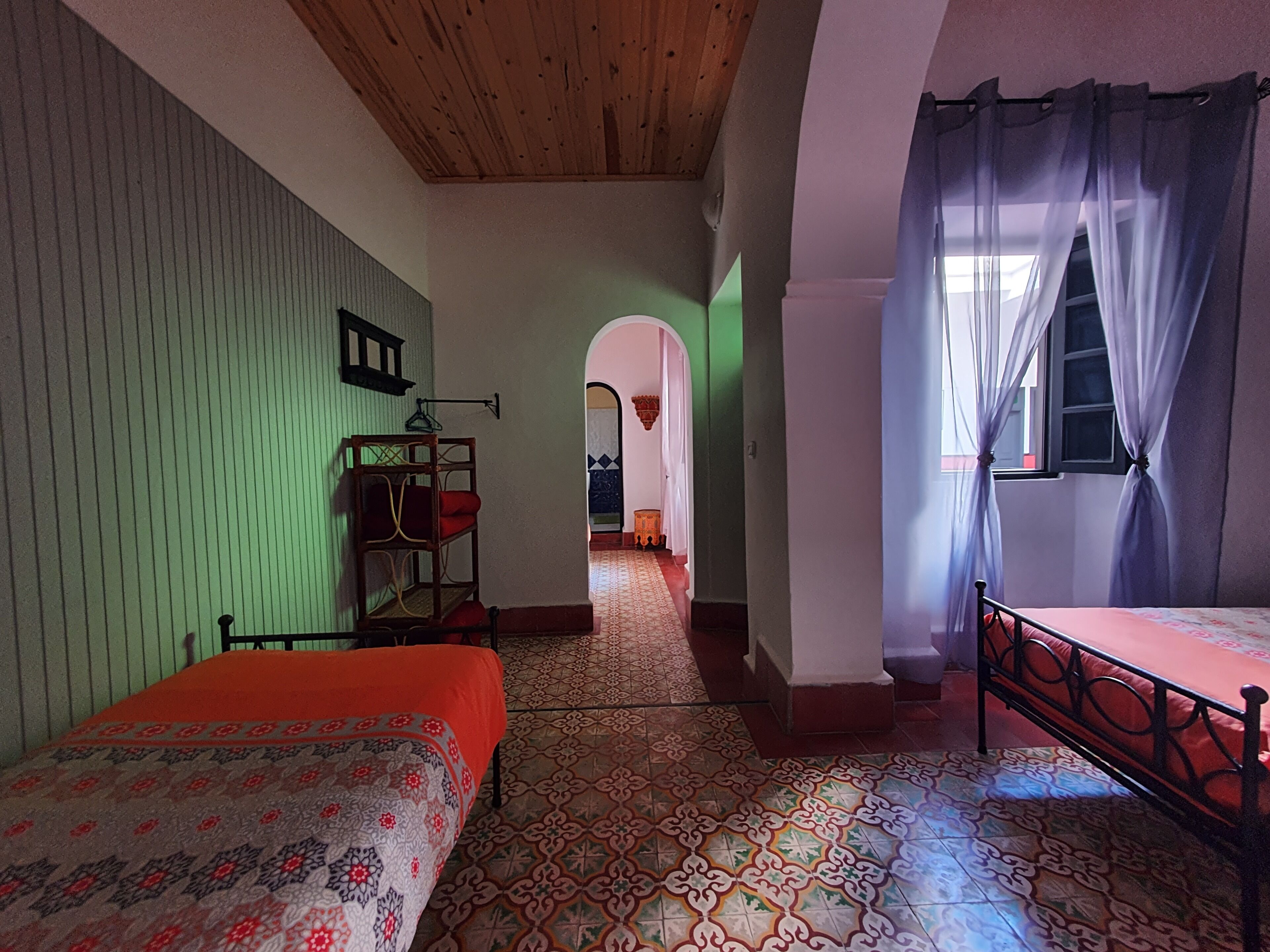 Una habitación con cama, techo de madera, piso estampado y ventana con cortinas.