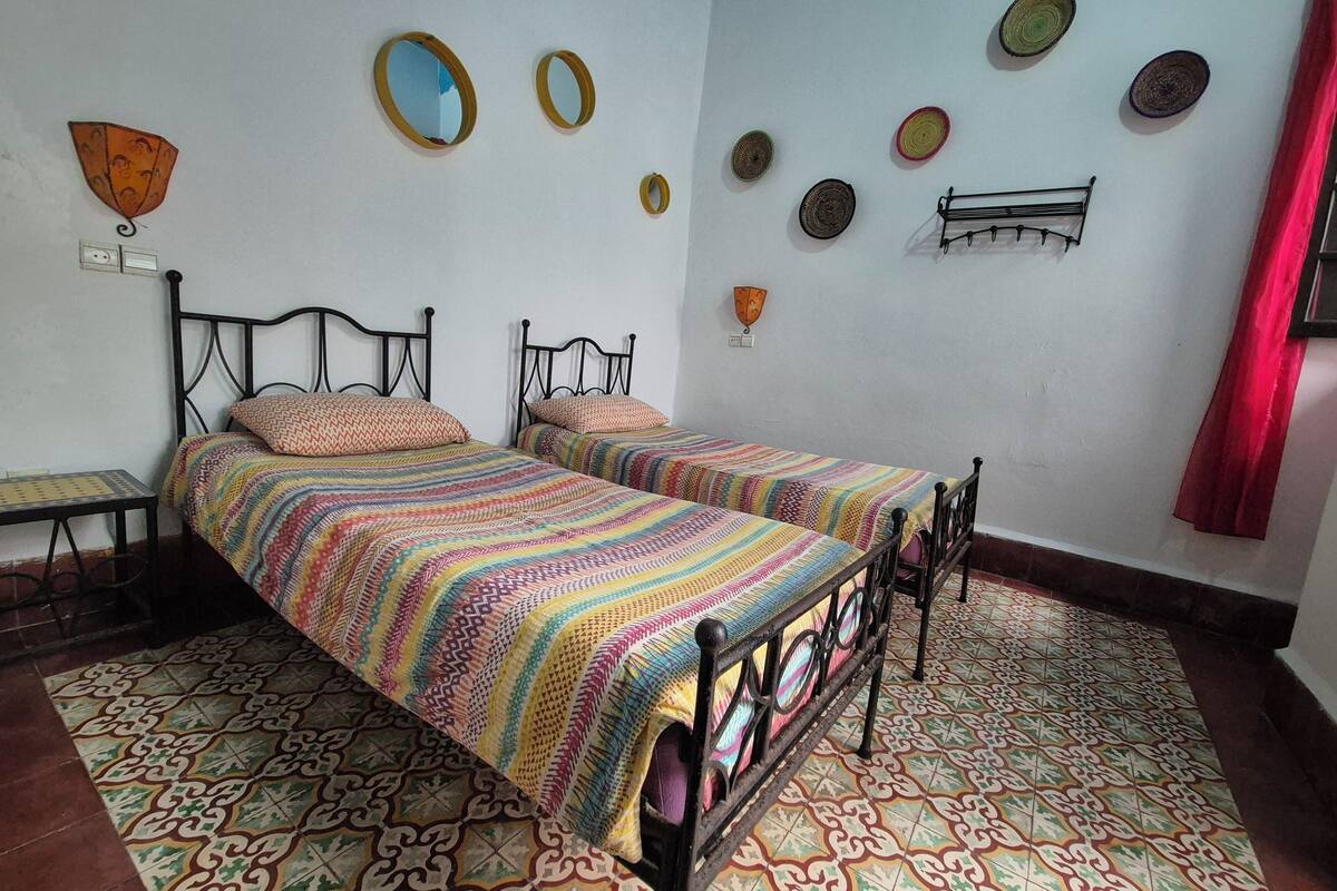 A room with two beds, patterned floor tiles, and wall decorations including mirrors and wall hangings.