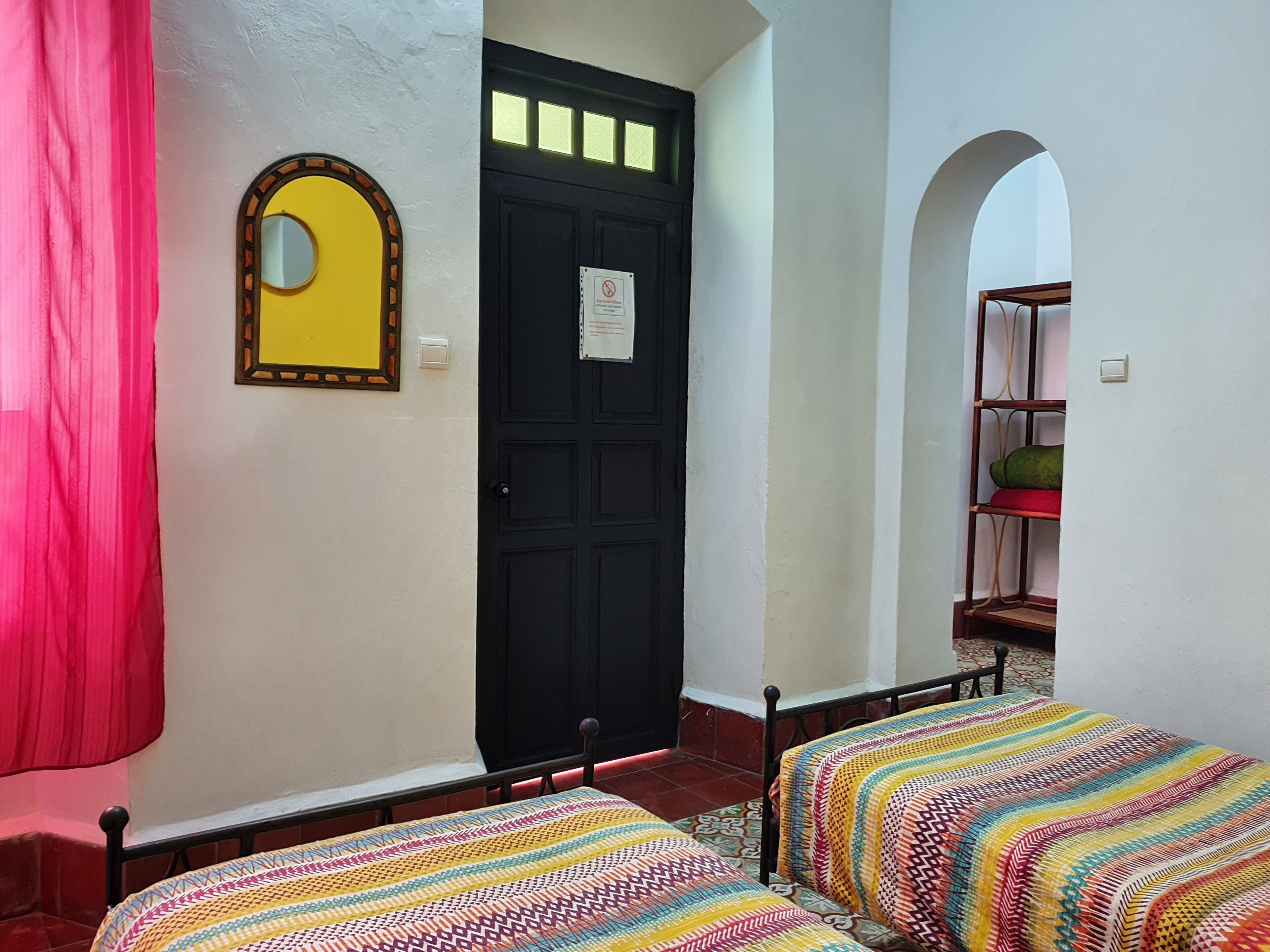 A room with a black door, a mirror, and two beds with colorful striped bedding.