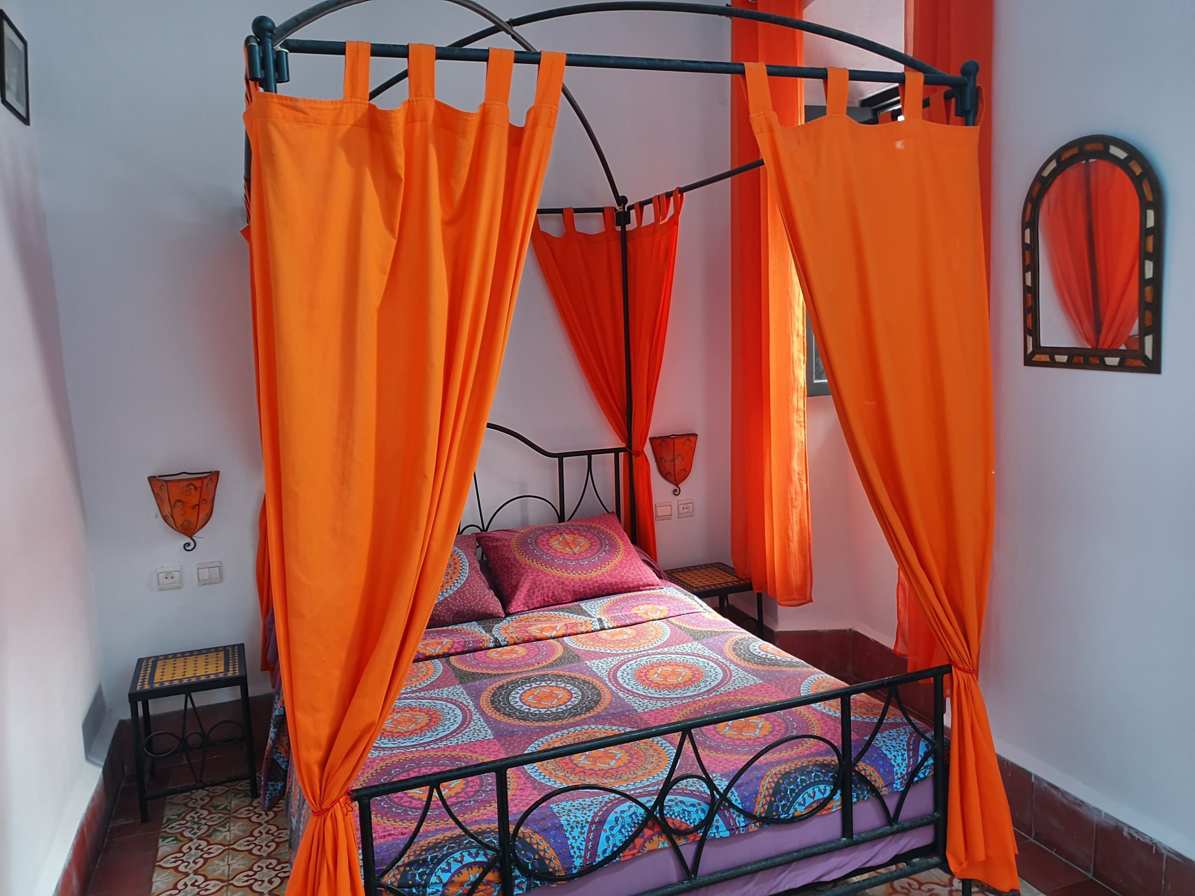 A bed with an orange canopy, patterned bedding, and a small bedside table.