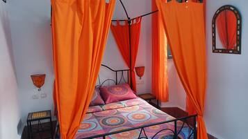 A bed with an orange canopy, patterned bedding, and a small bedside table.