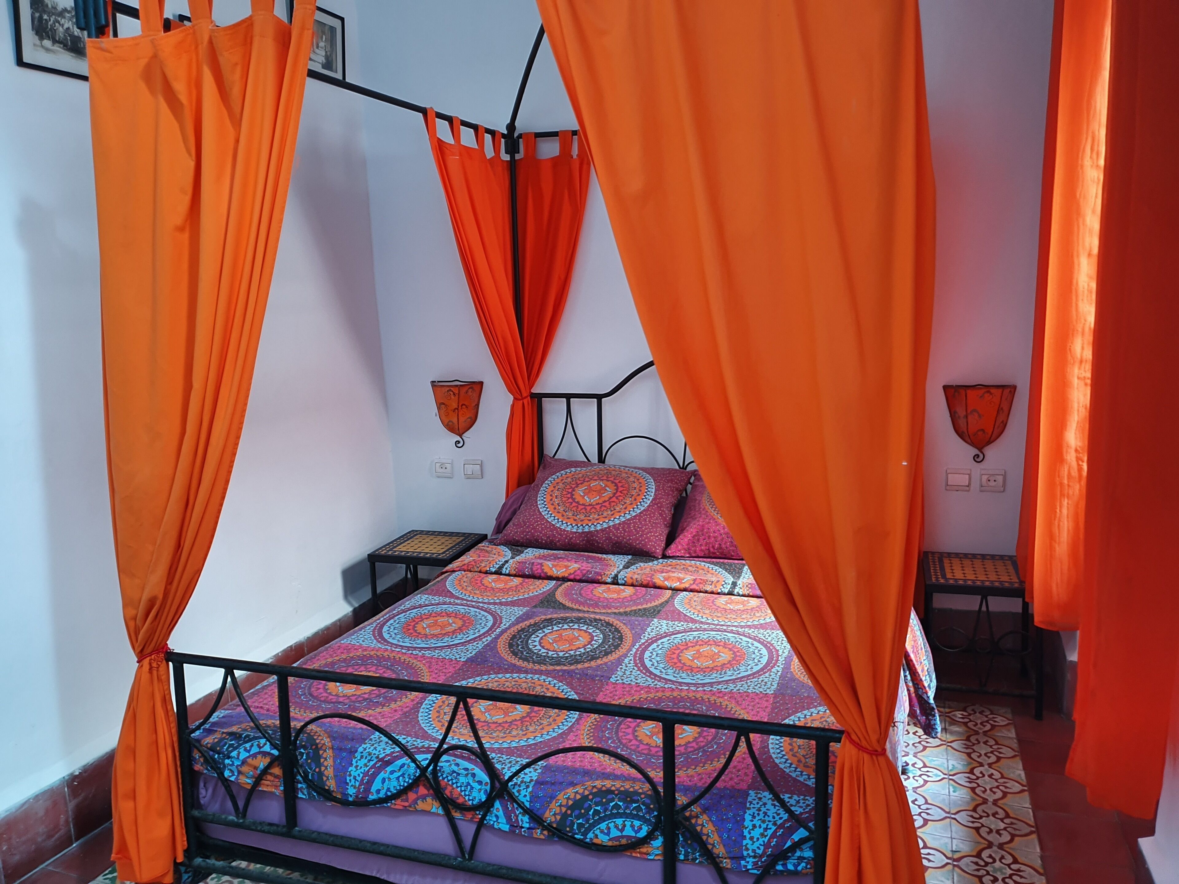A bed with an orange canopy, patterned bedding, and a small bedside table.