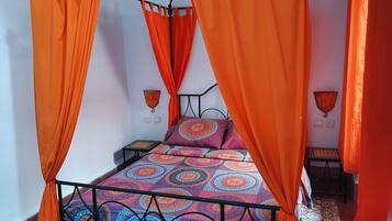 A bed with an orange canopy, patterned bedding, and a small bedside table.