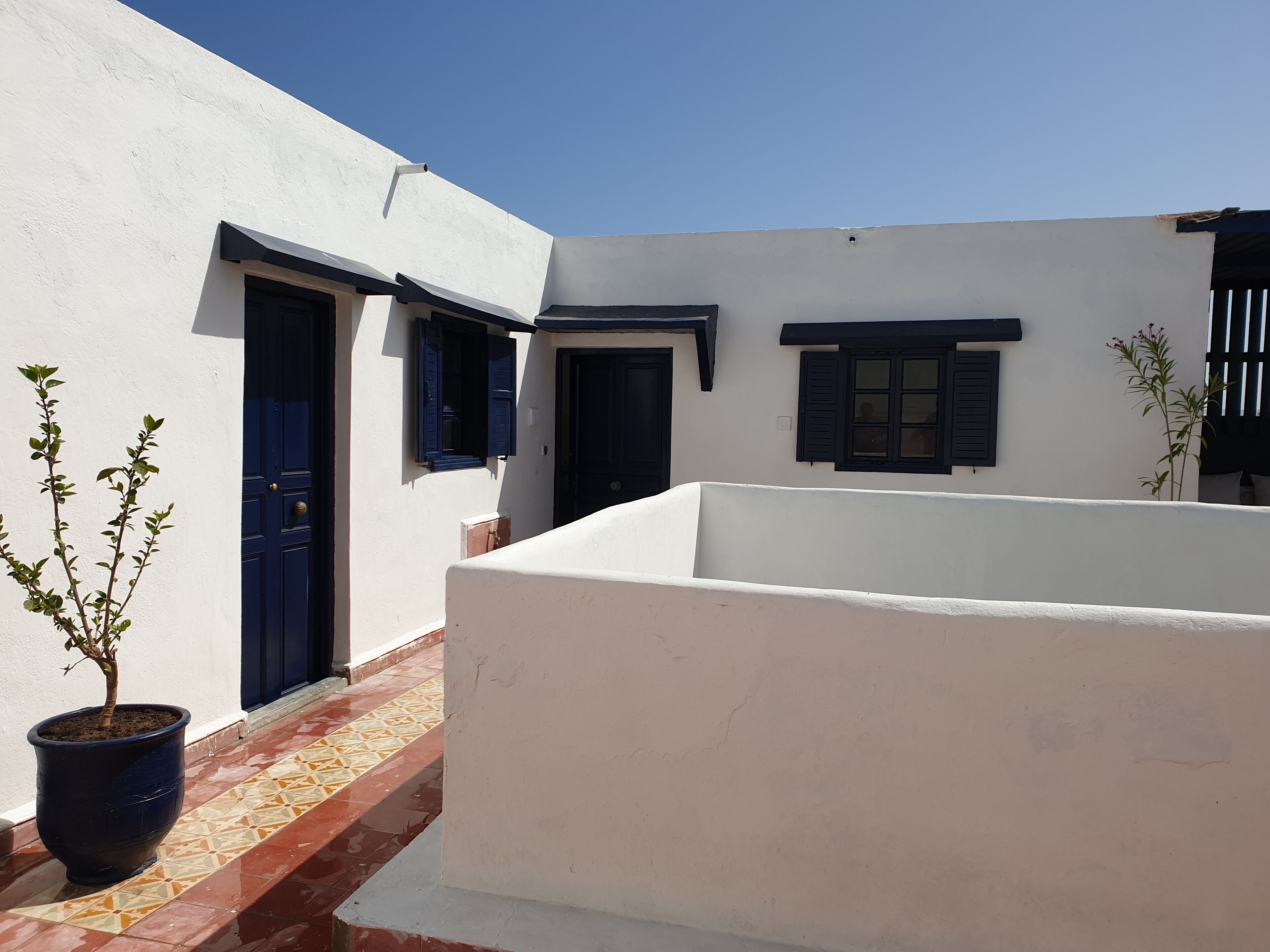 Un patio con un edificio blanco, una puerta azul y un suelo de baldosas.
