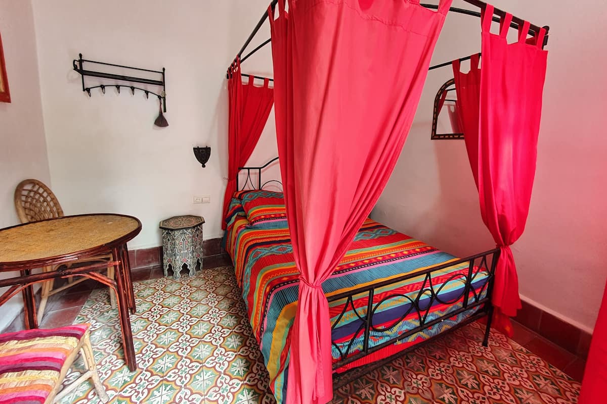 A room with a four-poster bed, a small round table, and a chair.