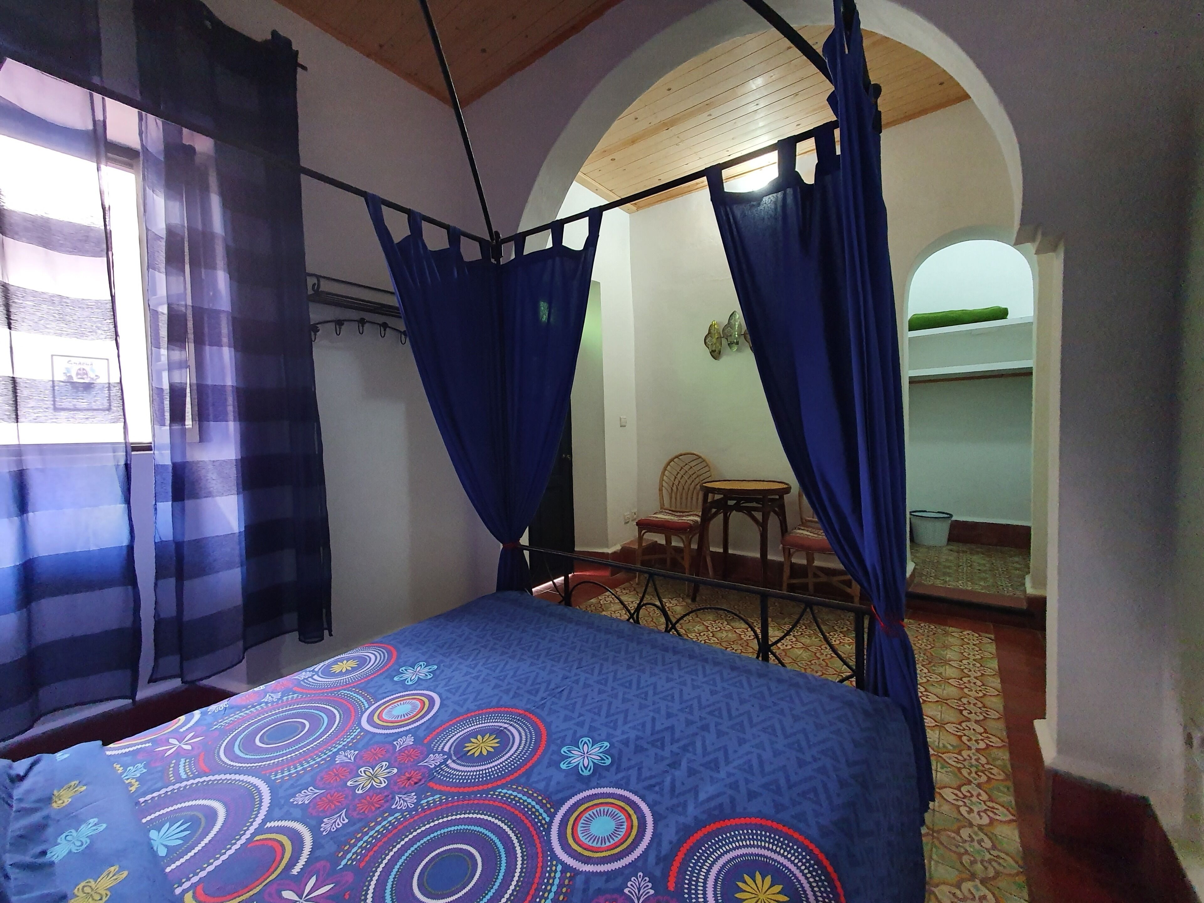 A bedroom with a bed, a chair, a small table, and a wardrobe.