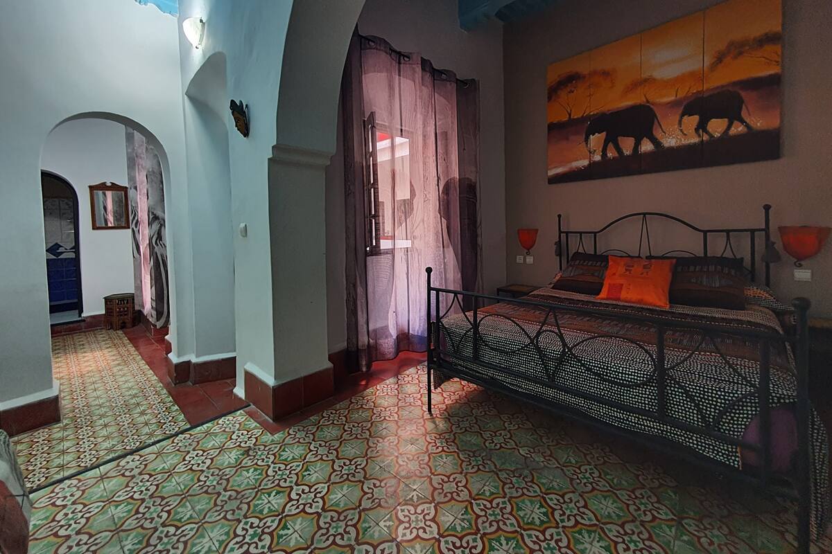 A room with a bed, patterned floor, and a painting of elephants.
