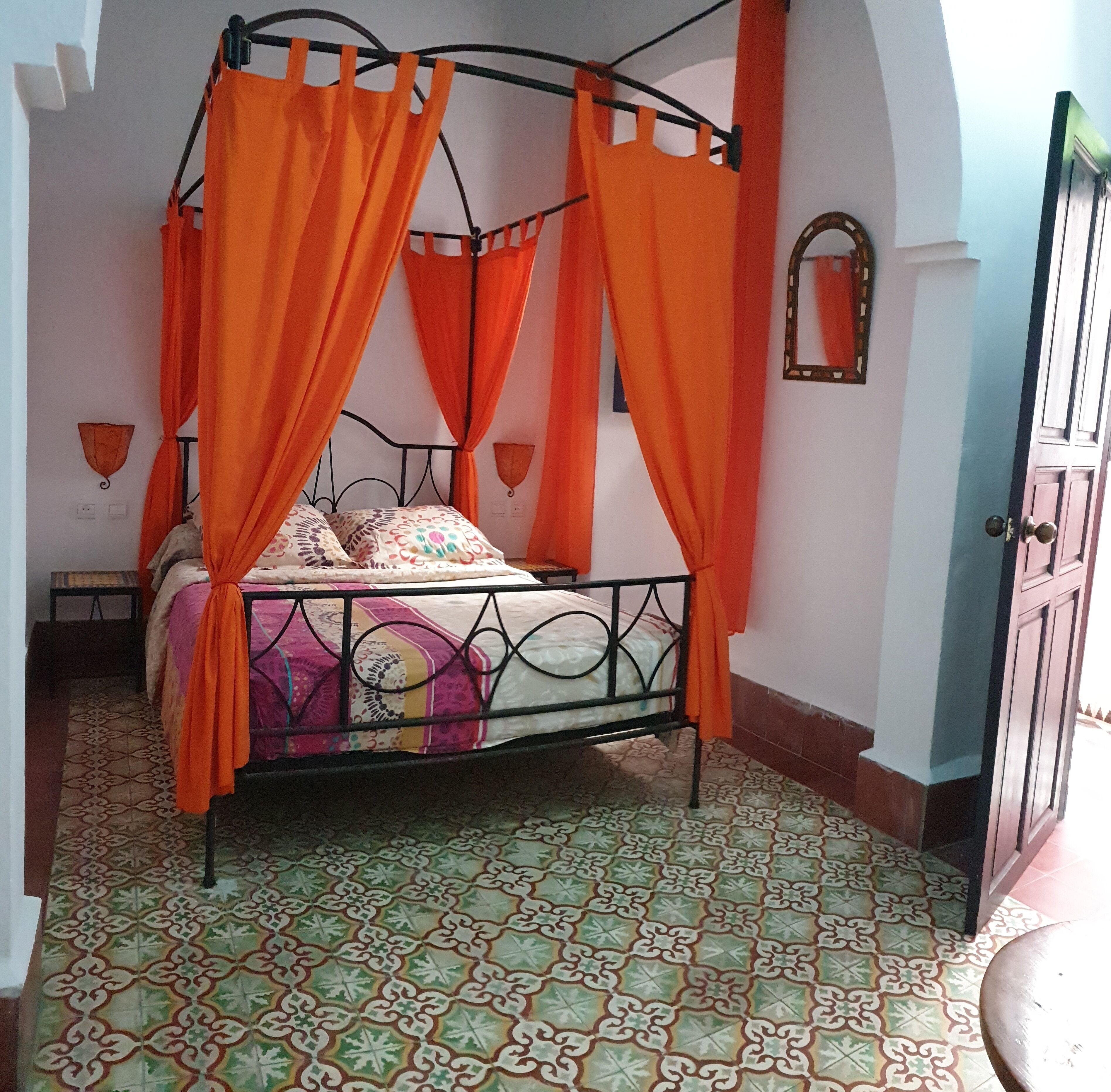 A bed with an orange canopy, a patterned floor, and a door to the right.
