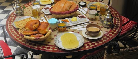A round table with a checkered tablecloth, surrounded by wicker chairs with red cushions.
