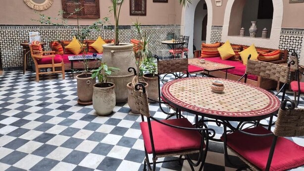 A checkered floor, outdoor seating with red cushions, and potted plants. - Riad Sidi Magdoul (Essaouira)