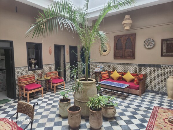 A cozy courtyard with a checkered floor, a sofa with colorful cushions, and several potted plants.