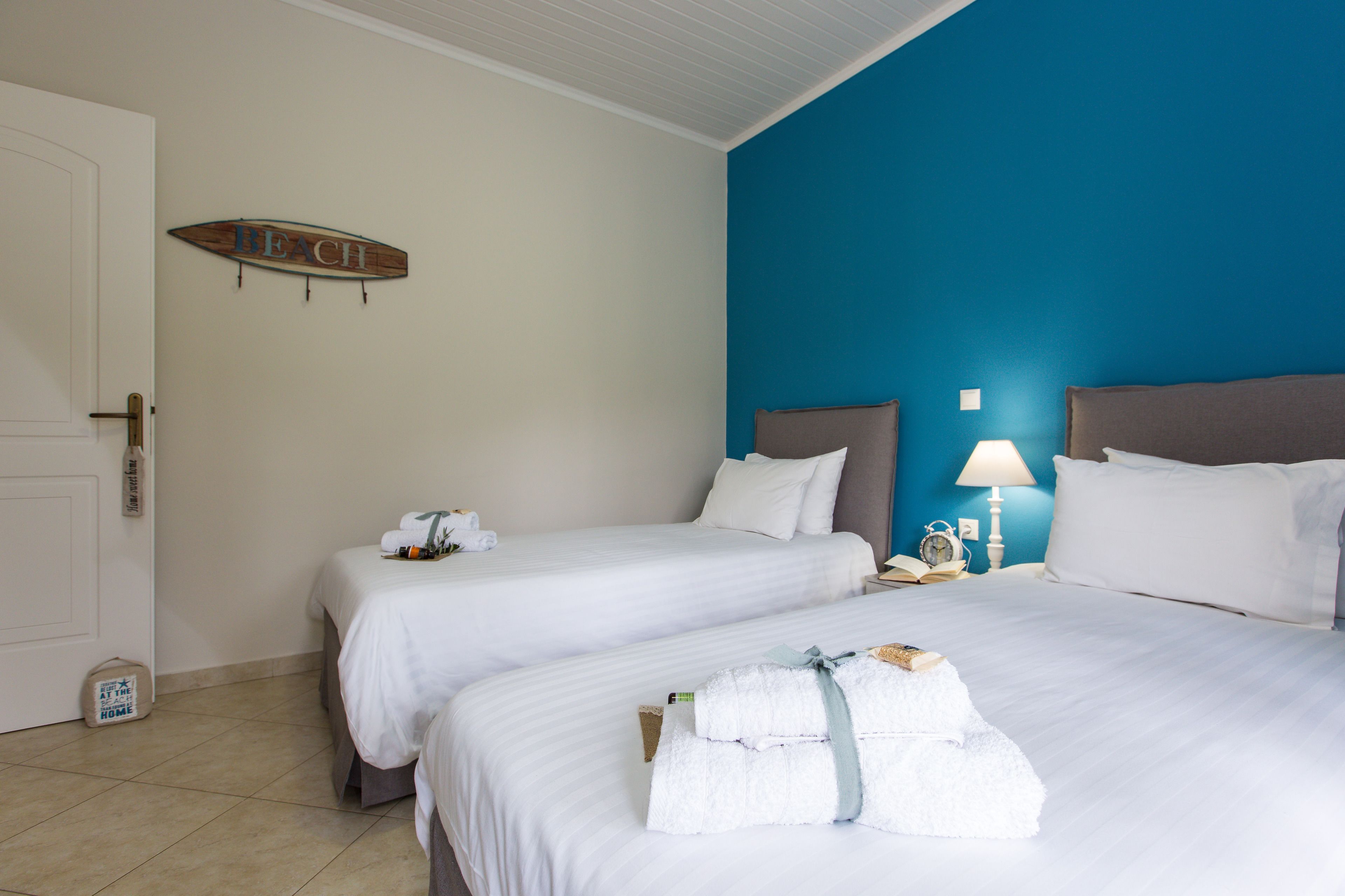 Ein Hotelzimmer mit zwei Betten, einem an die Form eines Surfbretts erinnernden Schild an der Wand und einer blauen Akzentwand.