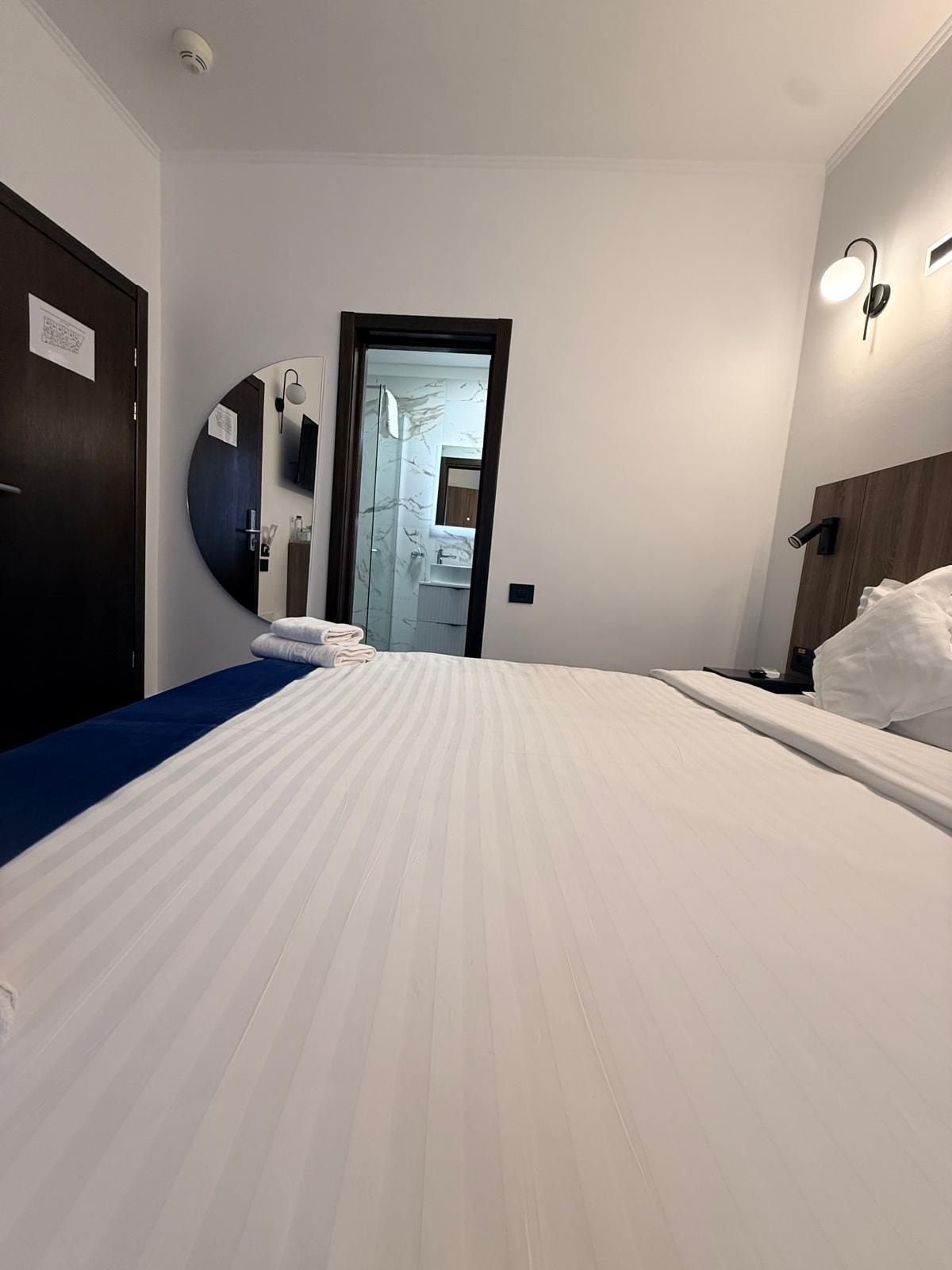 A hotel room with a large bed, a bedside table, a mirror, and a door leading to a bathroom.