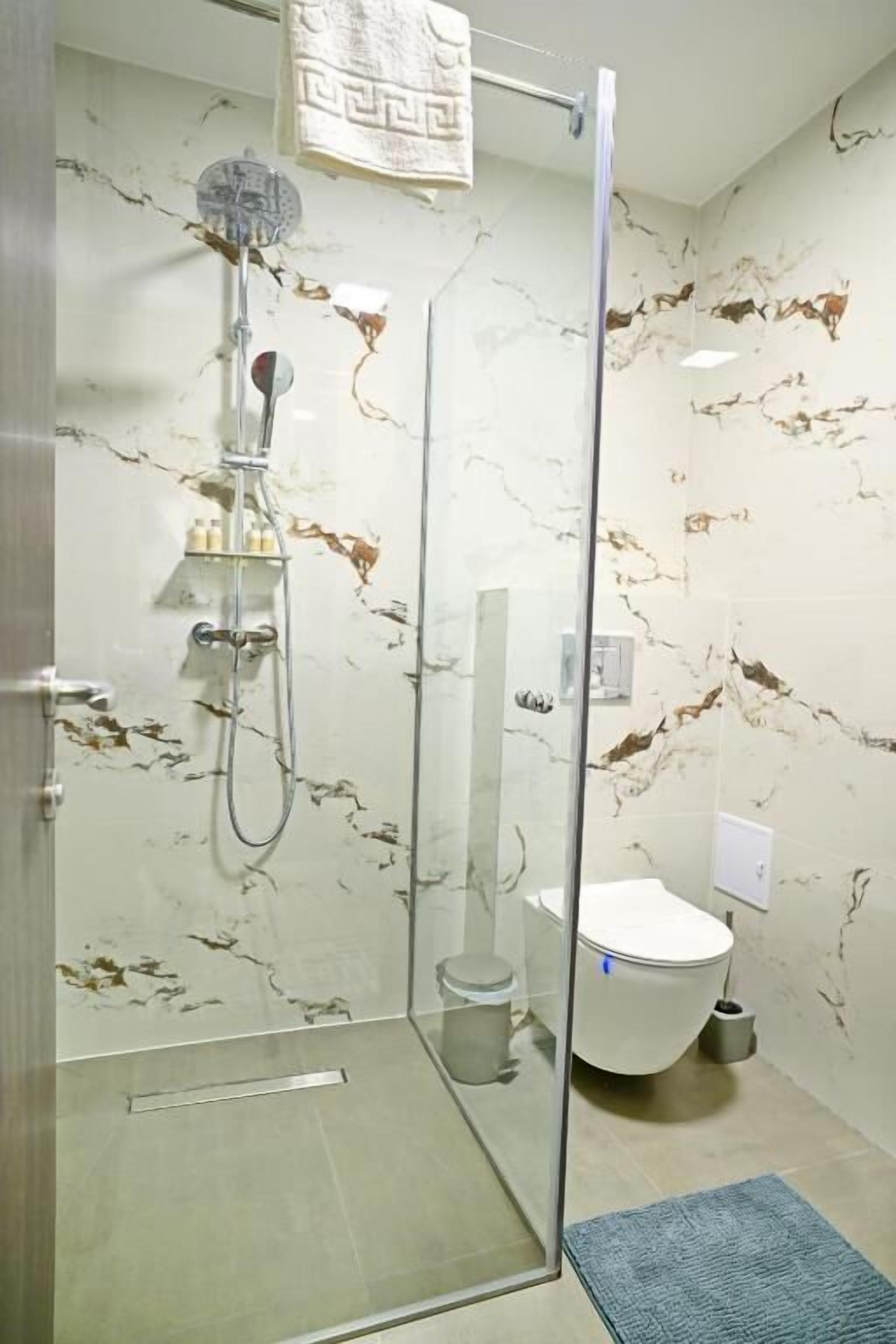 Une salle de bain dotée d’une douche à parois de verre, de toilettes et de murs aux motifs de marbre.