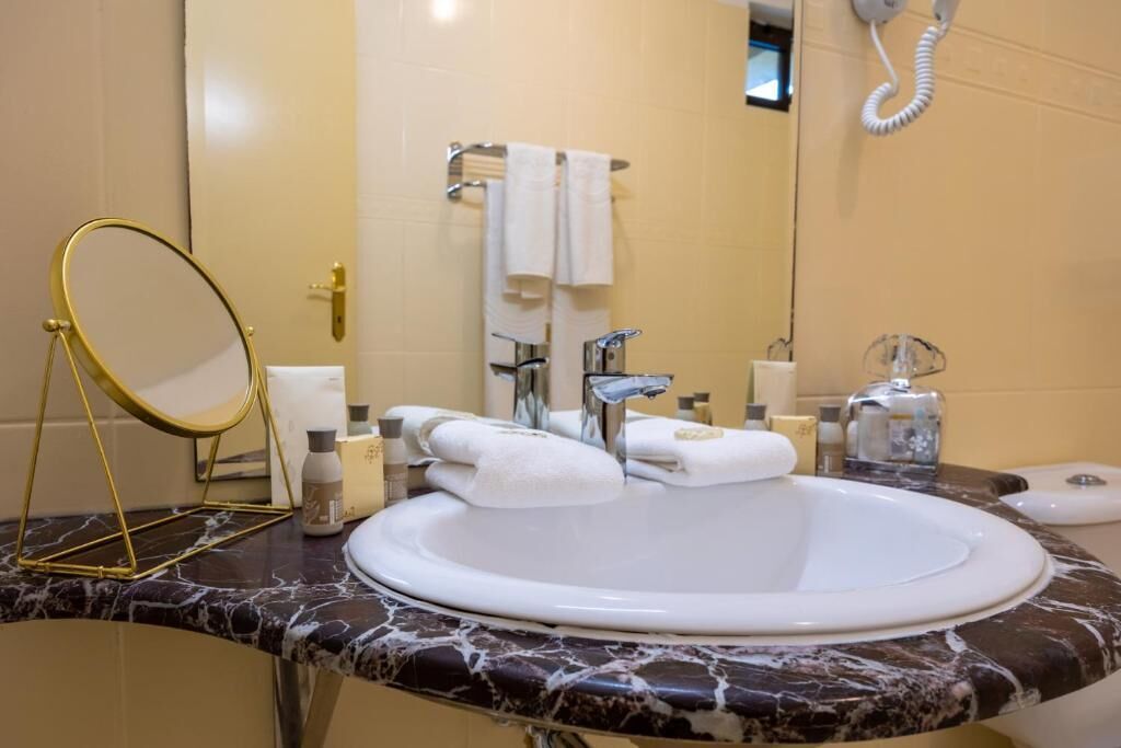 A bathroom with a marble sink, a gold-framed mirror, a towel rack with multiple towels, and a hand dryer.