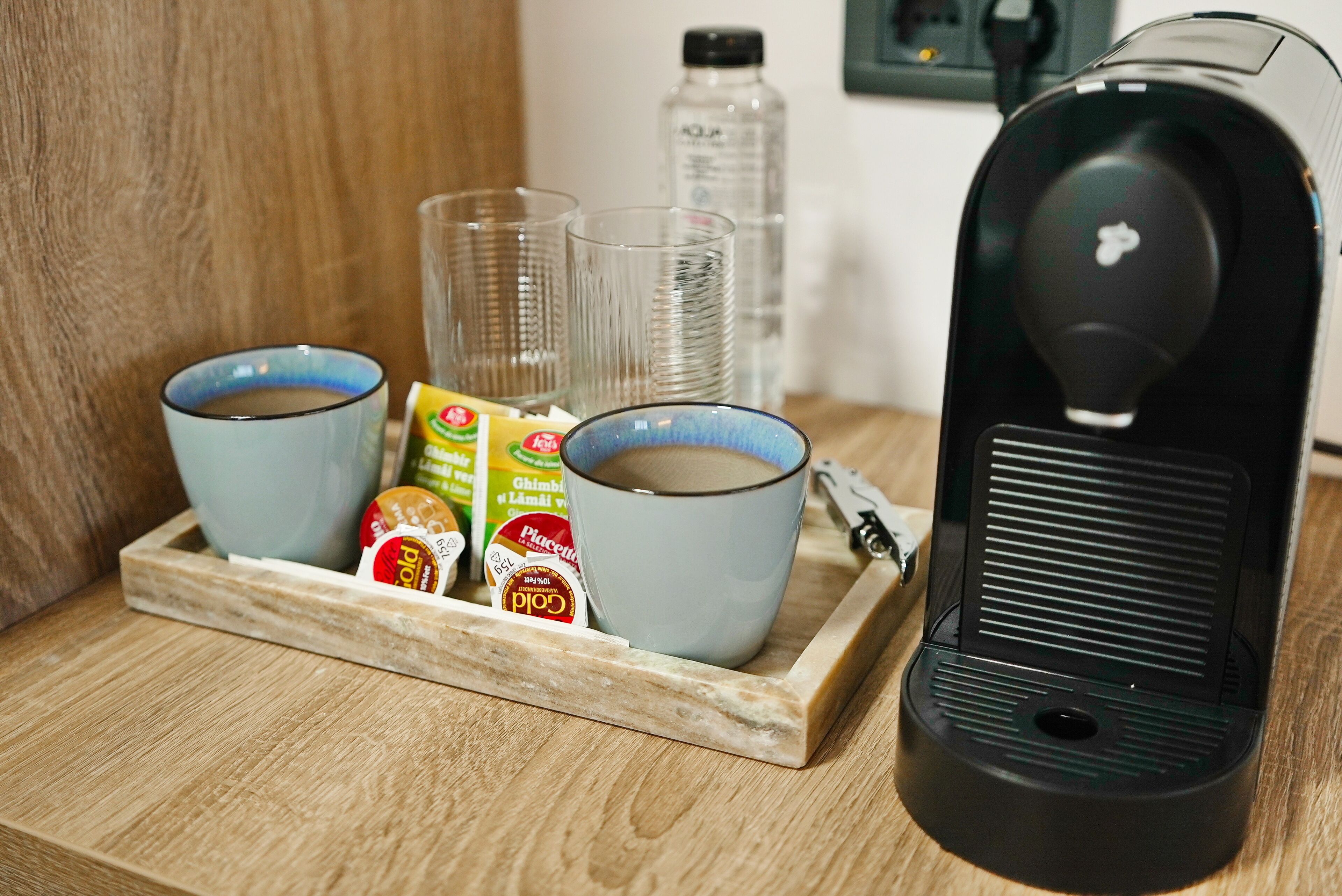 A coffee maker, two cups, and a tray with coffee pods and a bottle of water.
