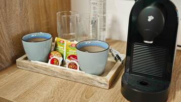 A coffee maker, two cups, and a tray with coffee pods and a bottle of water.