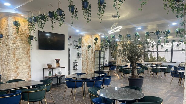 Un restaurante con mesas redondas y sillas azules, paredes de piedra y plantas colgantes.