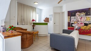 A modern living room with a dining area, a ceiling fan, and a vibrant painting on the wall. - Hotel Akti (Skiathos)