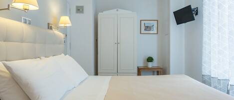 A hotel room with a bed, two wall-mounted lamps, a wardrobe, a small table with a plant, and a TV mounted on the wall.