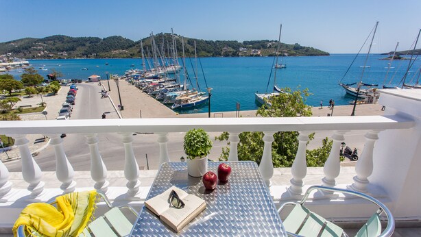 A balcony with a table, chairs, and a view of a marina with boats. - Hotel Akti (Skiathos)