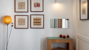 A wall with four framed artworks, a standing lamp, a mirror, and a small wooden table with decorative items. - Hotel Akti (Skiathos)