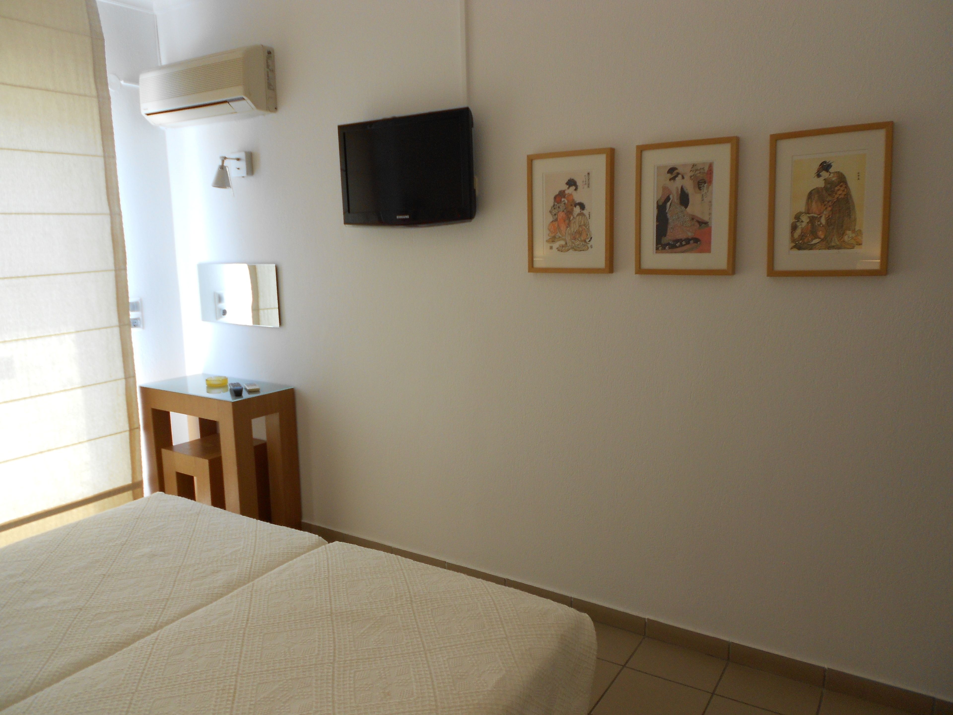A hotel room with a bed, a TV, a small table, and three framed pictures on the wall.