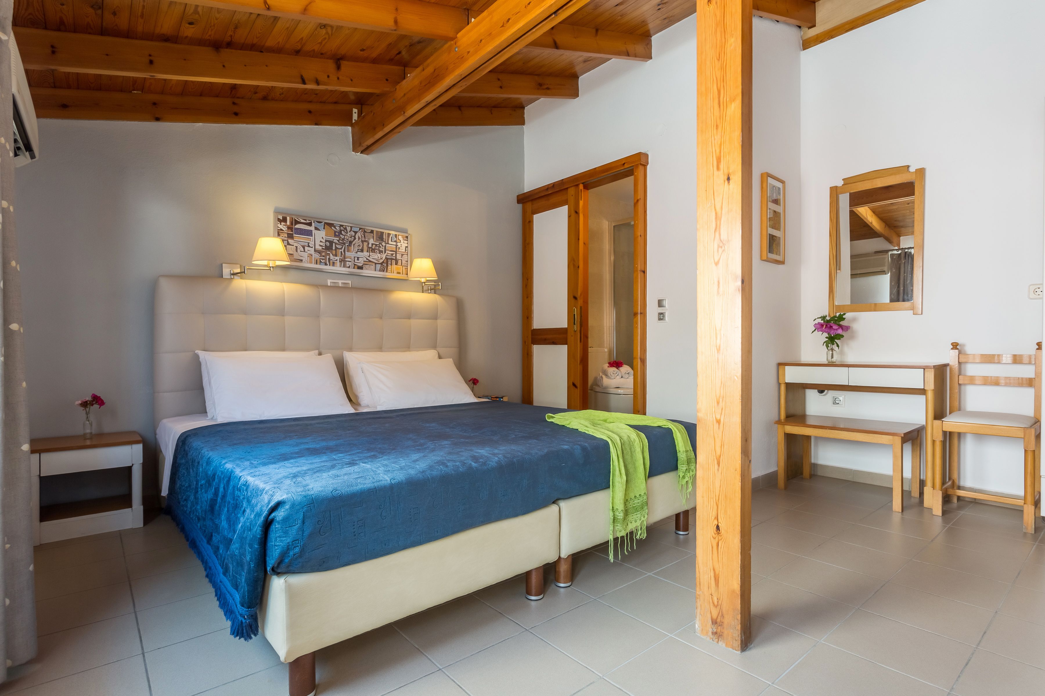 Un dormitorio con cama, mesita de noche, cómoda, espejo y techo de madera.