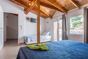 Ein Schlafzimmer mit einem Bett, Holzboden, Fernseher und einem Vorhangfenster.