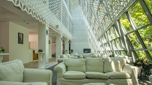 A spacious room with a high ceiling and intricate white lattice design. There are multiple seating areas with light-colored sofas and a round coffee table. - Zornitza Sands SPA (Elenite)