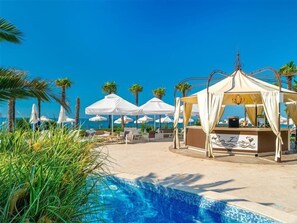 Un espace aménagé au bord de la piscine, avec des chaises longues, des parasols et un bar.