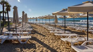 A beach with rows of white lounge chairs and beige umbrellas, arranged along the shoreline. - Zornitza Sands SPA (Elenite)