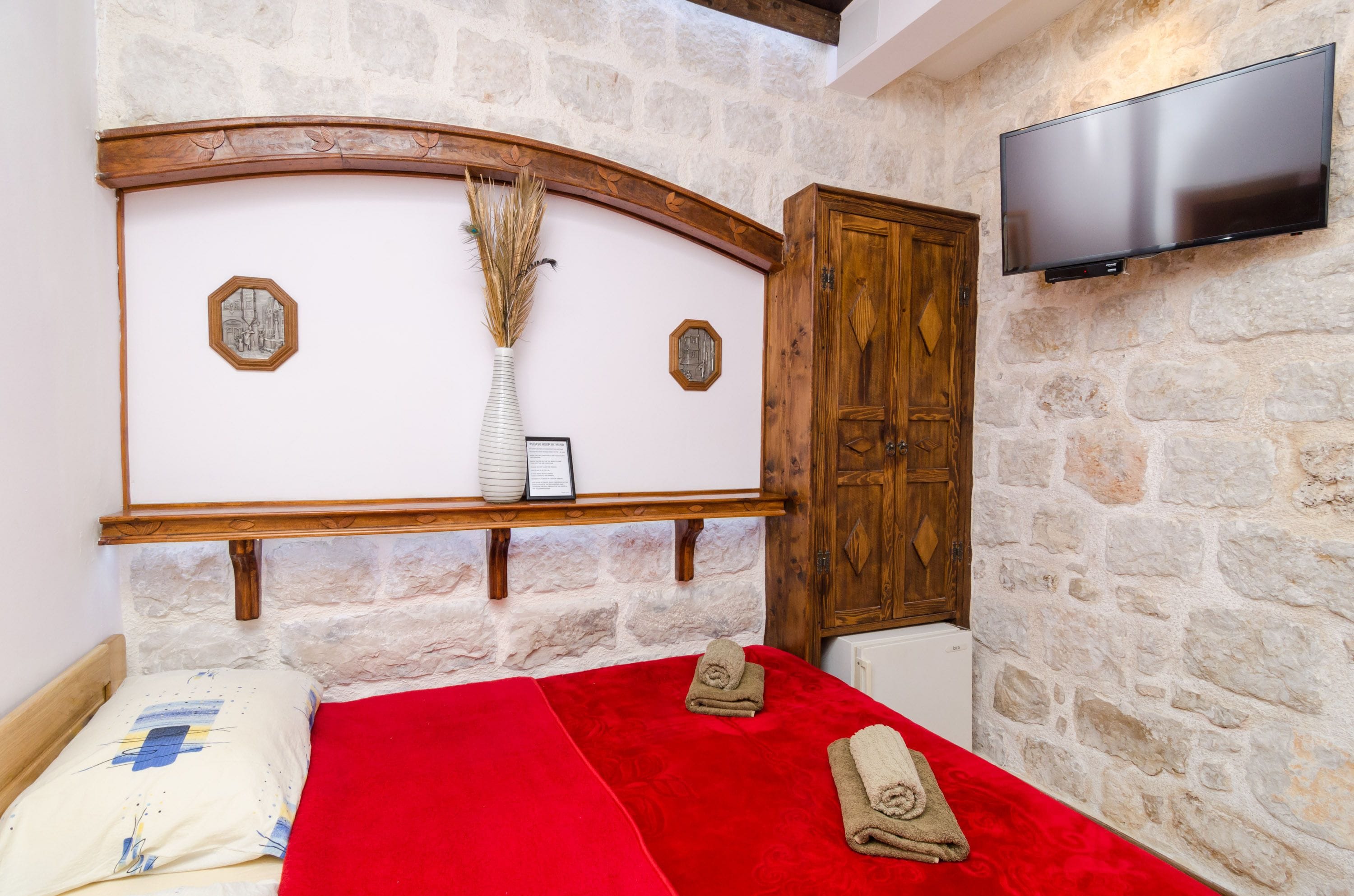 Une chambre avec un mur en pierre, une tête de lit en bois, un téléviseur à écran plat et une armoire en bois.