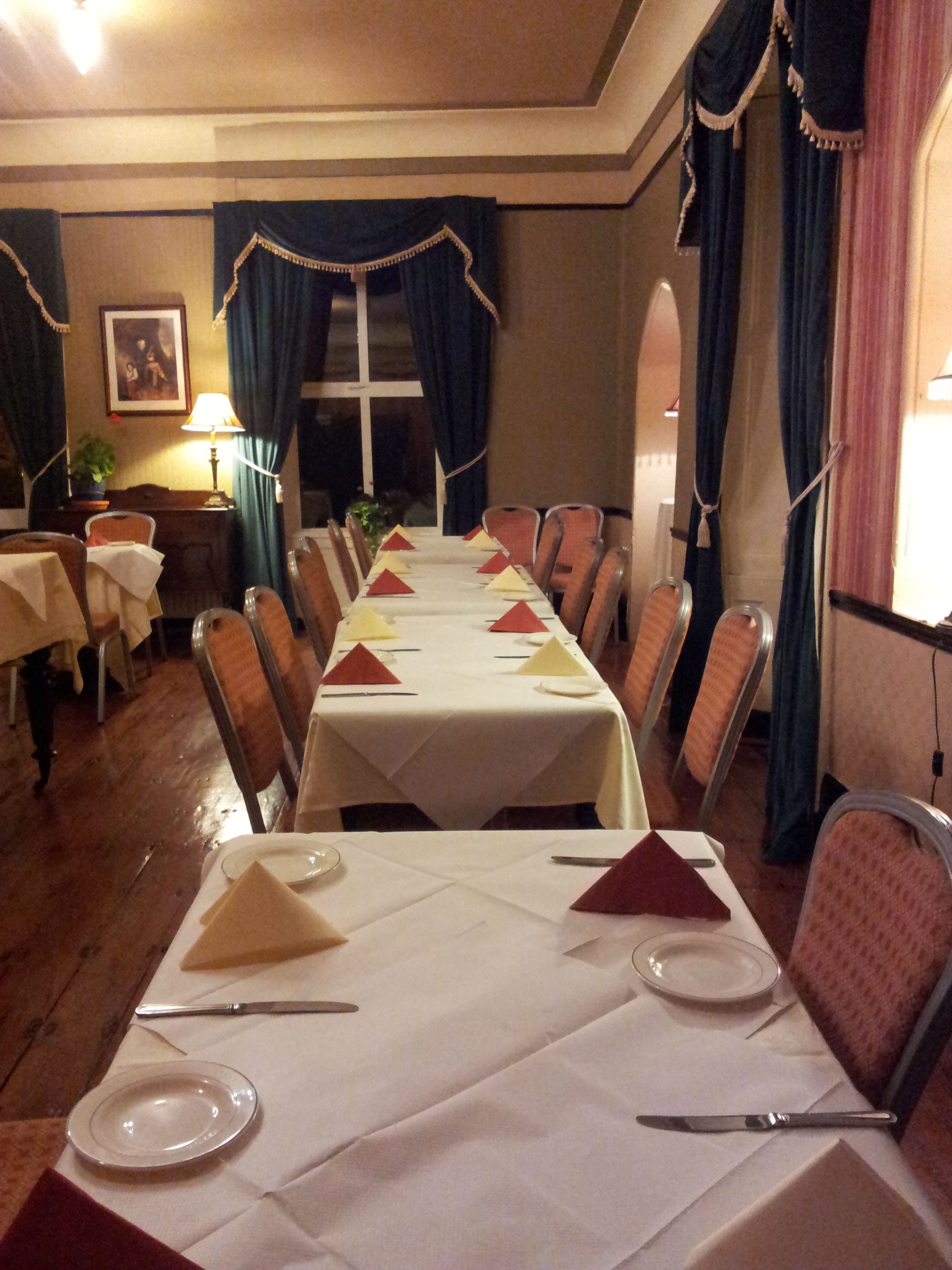 A dining area with a long table set for a meal, chairs, a lamp, and a window with curtains.