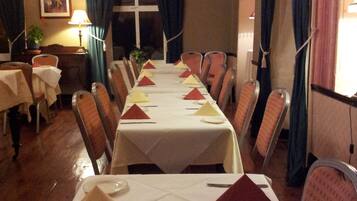 A dining area with a long table set for a meal, chairs, a lamp, and a window with curtains.