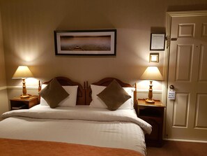 A hotel room with a bed, two bedside tables, two lamps, a framed picture on the wall, and a door with a 'Please Do Not Disturb' sign.