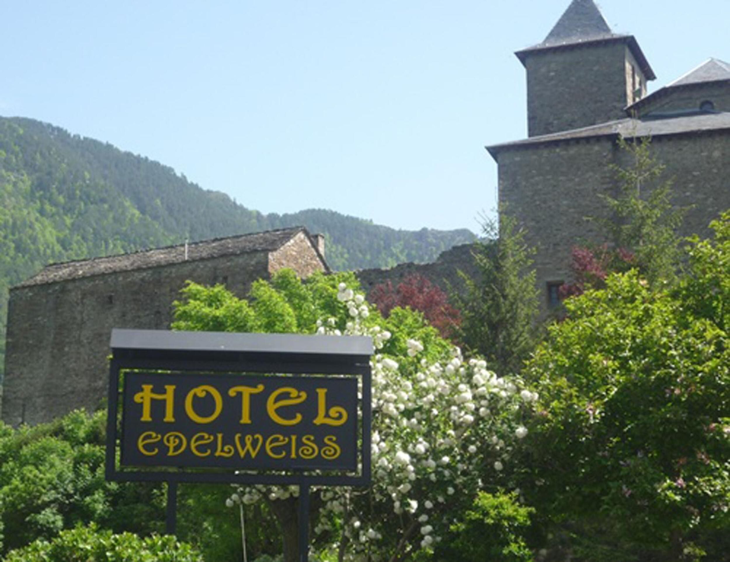 A sign for Hotel Edelweiss in front of a stone building with a tower.