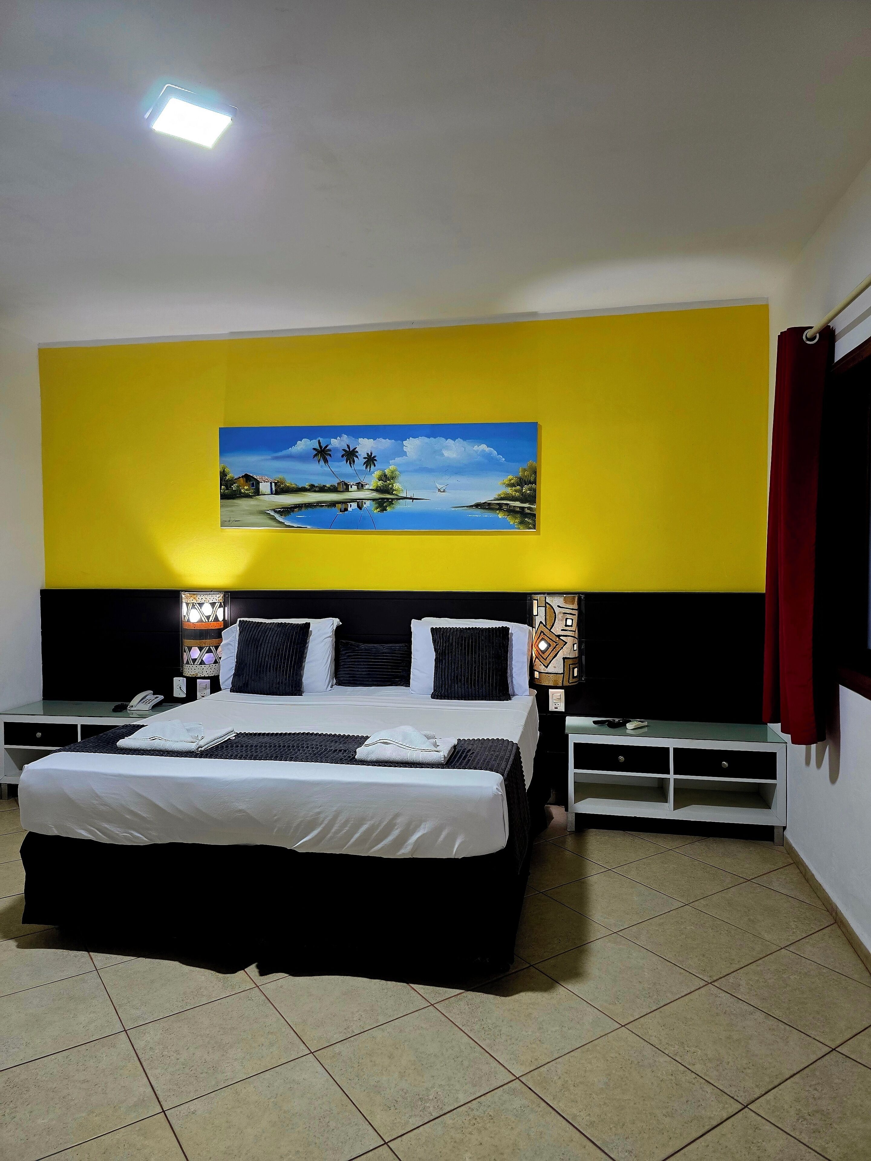 A bedroom with a bed, bedside tables, a painting, and a nightstand.