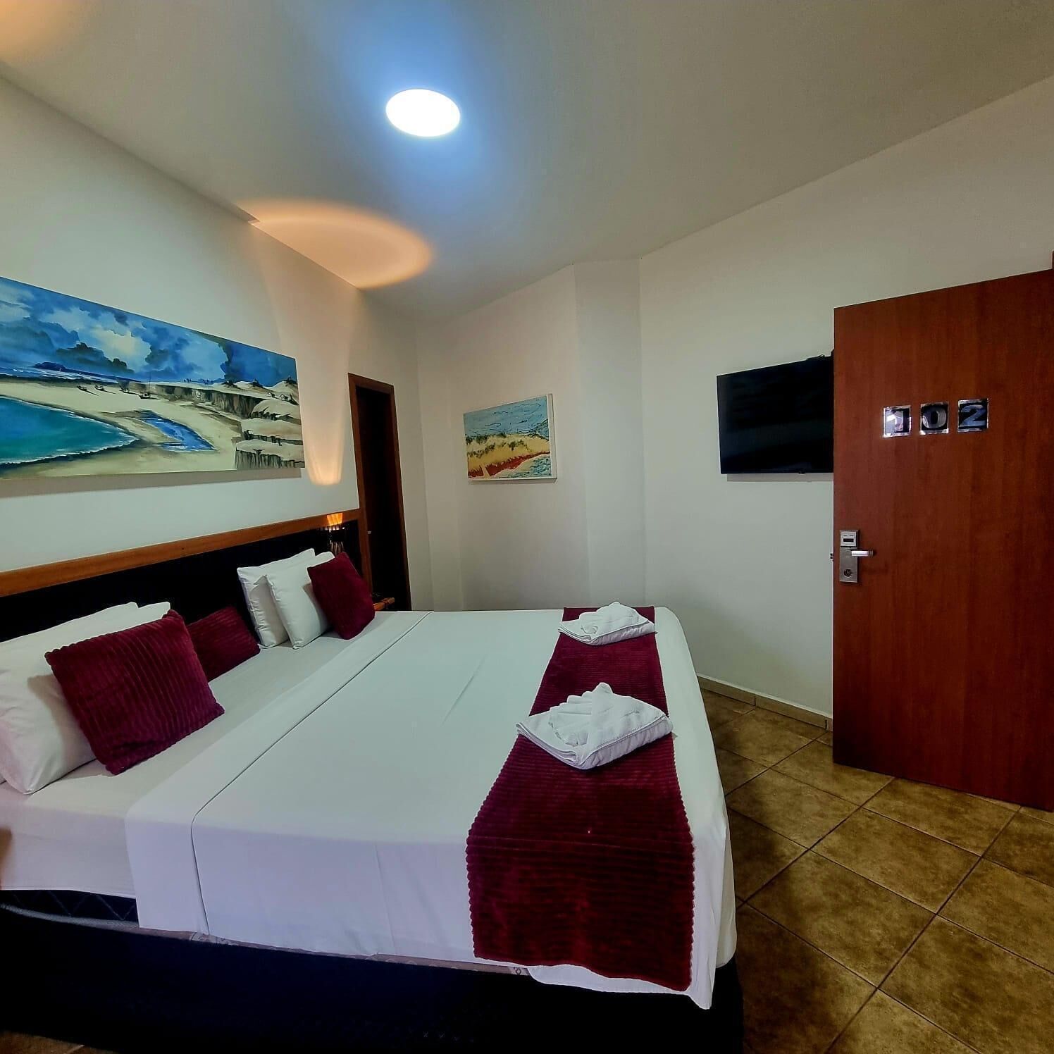 A hotel room with a bed, a TV, and two paintings on the wall.