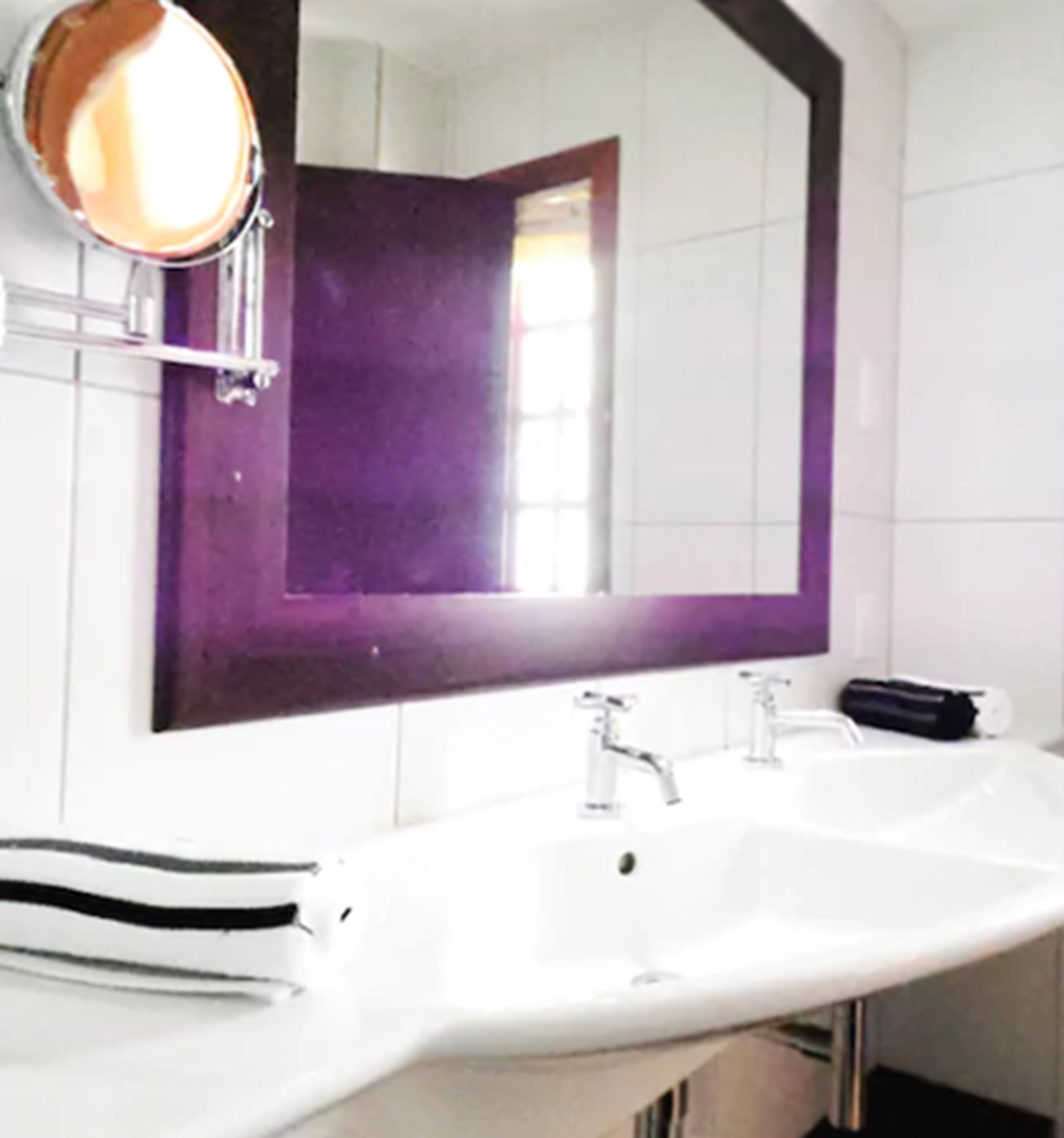 A bathroom with a white sink, a large mirror, and a purple-tiled wall.