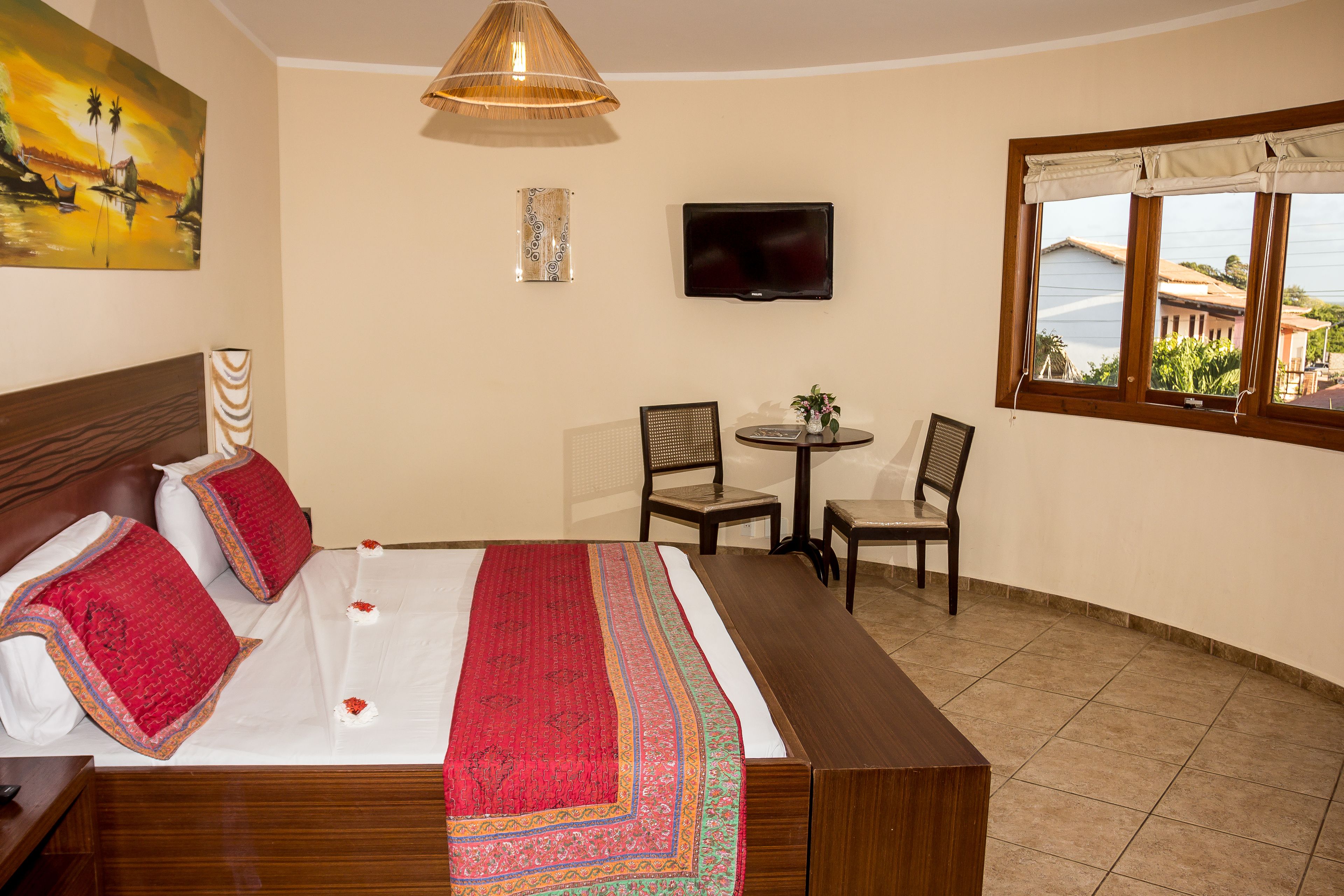 A hotel room with a bed, a TV, a dining area with chairs, and a window with a view.