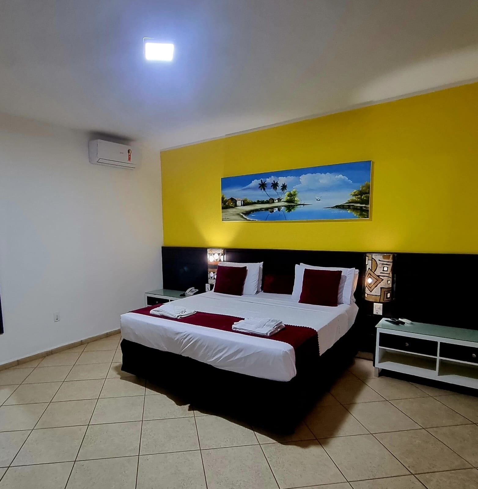 A hotel room with a bed, a nightstand, a TV, and a painting on the wall.