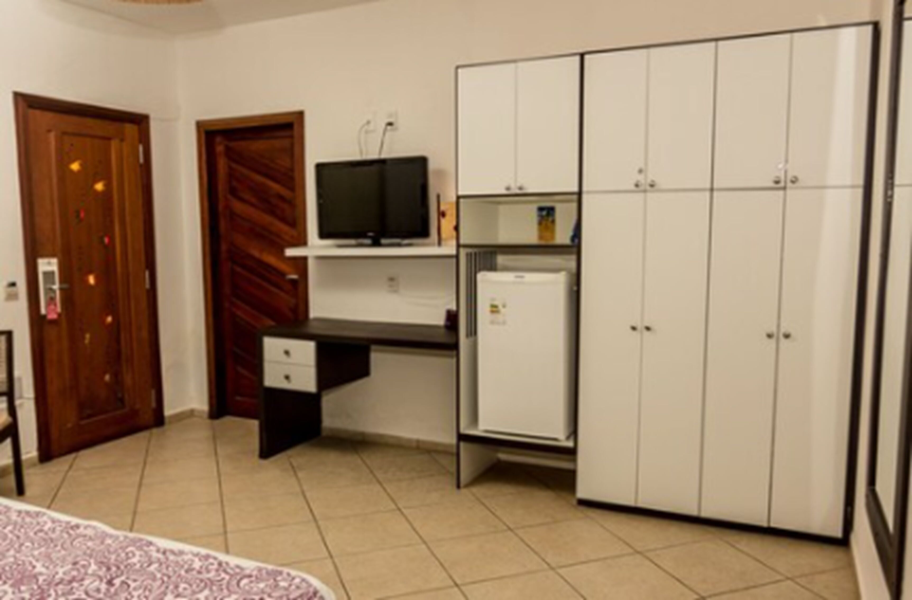 A bedroom with a bed, a desk with a computer, a television, and a wardrobe.