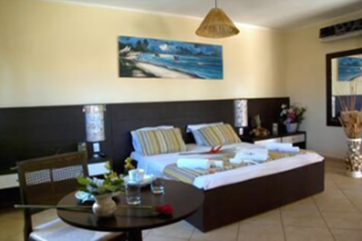 A bedroom with a bed, bedside tables, a round table with a vase, and a painting on the wall.