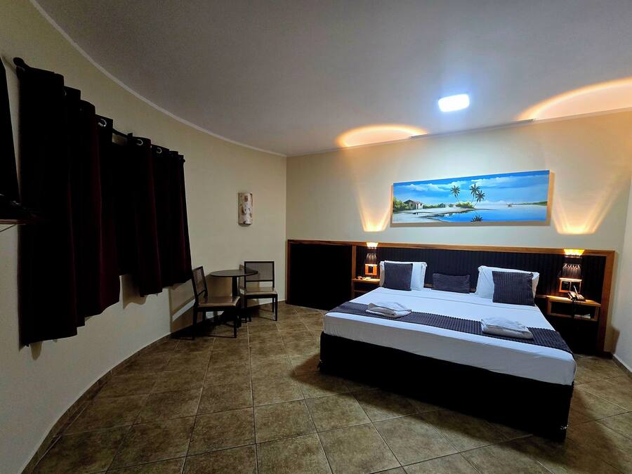 A hotel room with a large bed, a desk, a chair, and a painting on the wall.