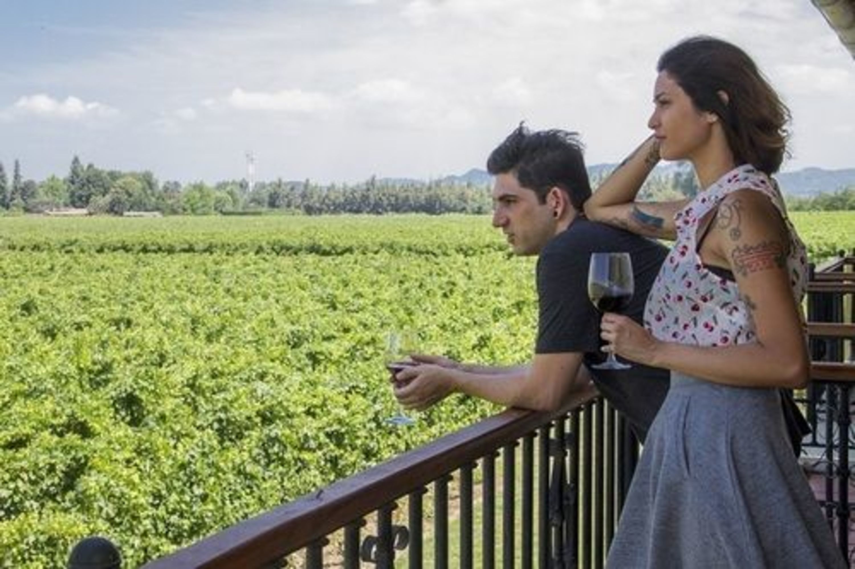 Una pareja parada en un balcón con vistas a un viñedo.